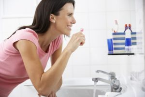 Woman smiling in the mirror while brushing her teeth