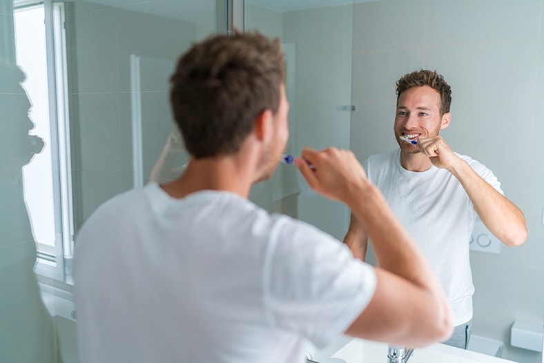 Man brushing teeth in mirror